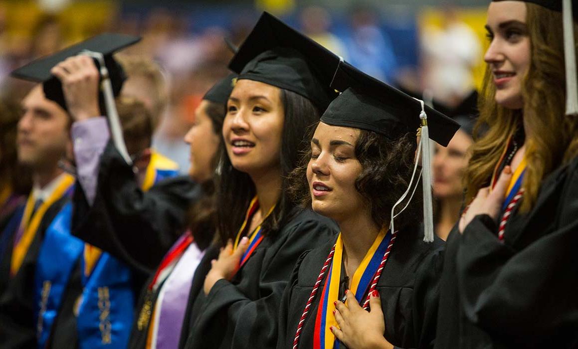 学生们戴着毕业帽，身穿毕业服，双手放在胸前站立